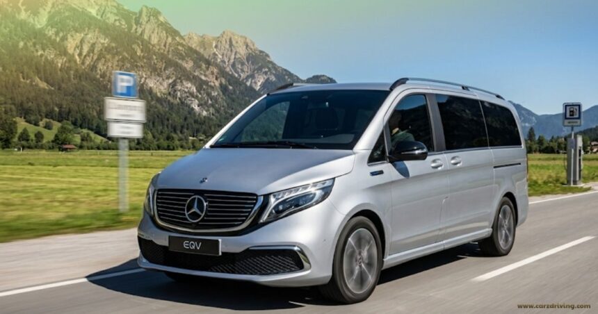 A silver Mercedes-Benz EQV 7-seater electric van driving on a scenic road with a background of green fields and rocky mountains under a blue sky.