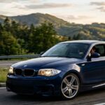 Blue BMW 135i sports coupe driving on a scenic road with mountain background.