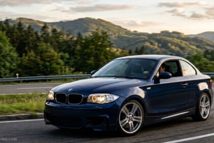 Blue BMW 135i sports coupe driving on a scenic road with mountain background.
