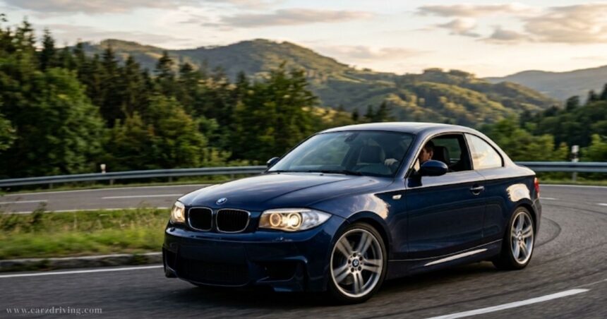 Blue BMW 135i sports coupe driving on a scenic road with mountain background.