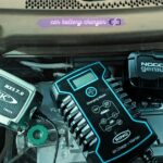 Collection of CTEK, Ring, and NOCO smart car battery chargers placed on a vehicle battery inside an engine compartment.