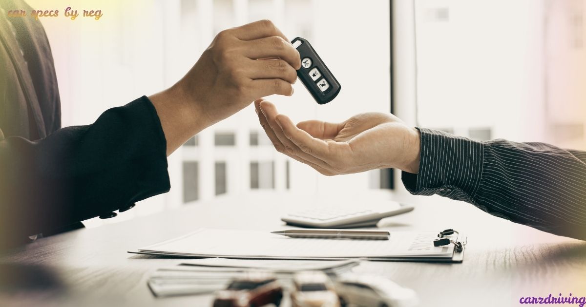 Close-up of a person handing over a car key fob to another person over a desk with paperwork, illustrating a vehicle handover or checking car specs by reg.