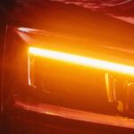Close-up of a modern car with LED amber daytime running lights glowing on a sleek red vehicle exterior at night