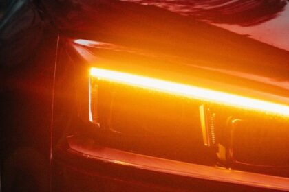 Close-up of a modern car with LED amber daytime running lights glowing on a sleek red vehicle exterior at night