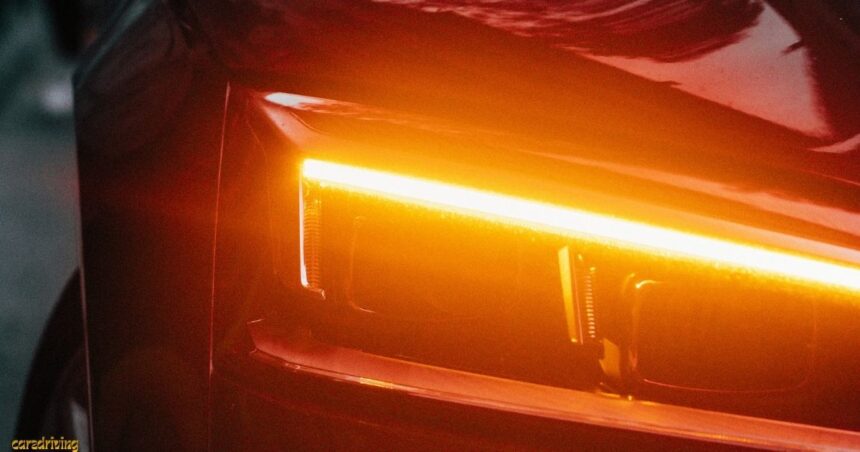 Close-up of a modern car with LED amber daytime running lights glowing on a sleek red vehicle exterior at night