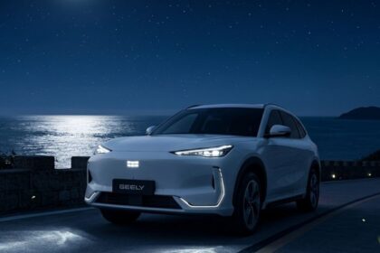 White Geely EX5 electric SUV parked on a road at night next to the ocean.