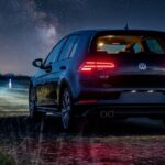 Rear view of a dark Volkswagen Golf GTE parked outdoors at night under a starry sky and a bright crescent moon.