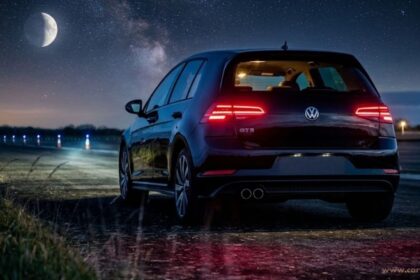 Rear view of a dark Volkswagen Golf GTE parked outdoors at night under a starry sky and a bright crescent moon.