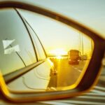 Golden hour reflection of a highway and truck in a passenger side mirror car blind spot view.
