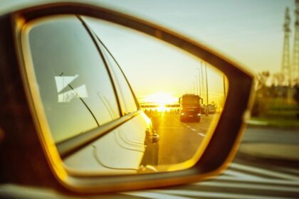 Golden hour reflection of a highway and truck in a passenger side mirror car blind spot view.