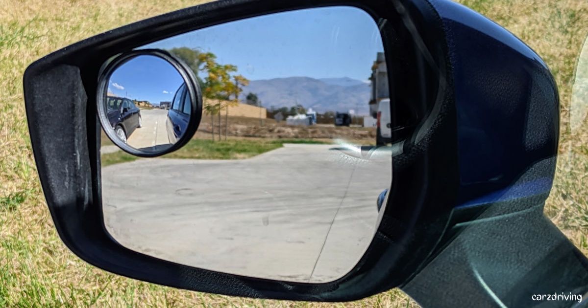 Close-up of a side wing mirror car blind spot attachment showing a wide-angle view of a road with vehicles behind.