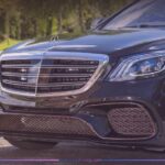 Close-up front view of a black Mercedes-AMG S65 luxury sedan featuring a chrome grille, distinctive LED headlights, and custom bronze multi-spoke alloy wheels parked outdoors.