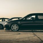 Three modified cars parked on an airfield at sunset, ideal for drivers looking for a guide on how to sorn my car in the UK.