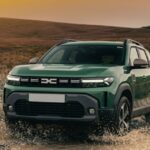 A green Dacia Duster driving off-road and splashing water on a dirt track.