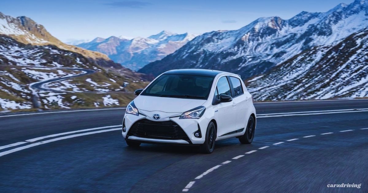 "White Toyota Yaris GR Sport hatchback driving on a mountain road with snow-capped peaks in the background"