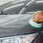 Person using a dual-action buffer machine to apply car polish onto a dark vehicle hood