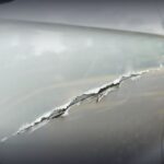 Close-up of a deep gash and paint damage on a silver car door, illustrating the need for professional car scratch repair near me