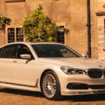 Alpina BMW luxury sedan parked in front of a classic home, showcasing signature multi-spoke wheels.