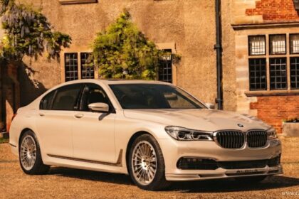 Alpina BMW luxury sedan parked in front of a classic home, showcasing signature multi-spoke wheels.