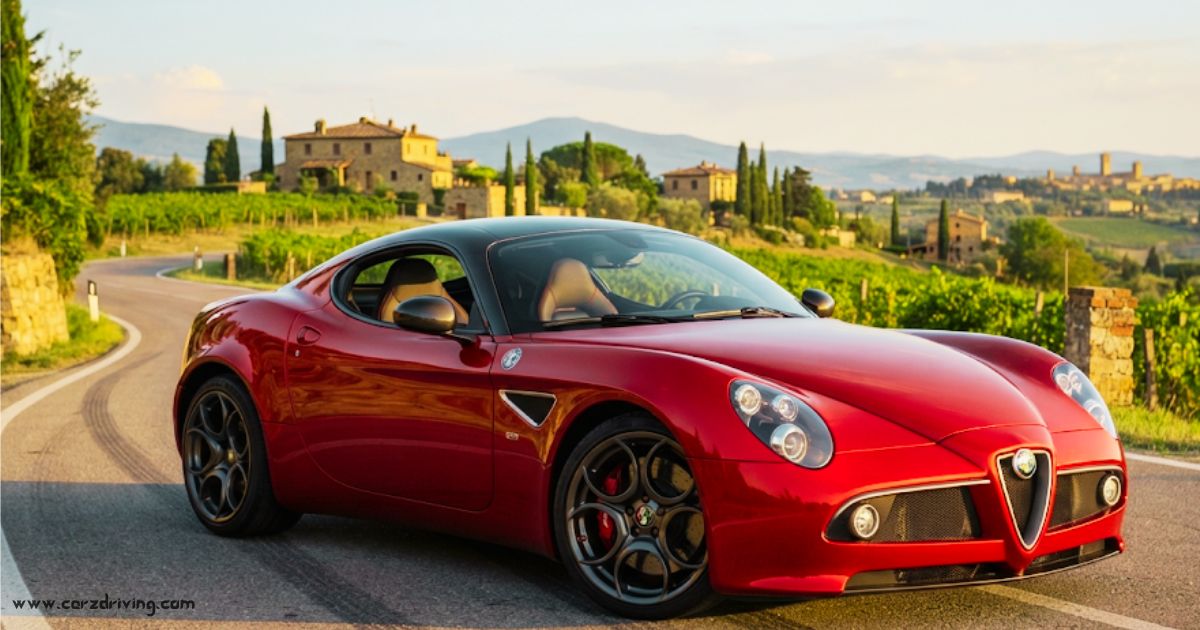A red Alfa Romeo 8C Competizione sports car parked on a winding road in the Italian countryside, surrounded by vineyards and historic buildings at sunset.