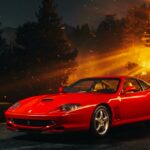 A red Ferrari 550 Maranello parked on a dark road at night, illuminated by the bright, fiery orange glow of a nearby wildfire in the background.