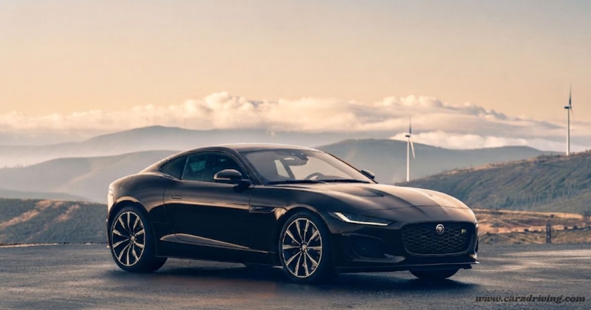 "Sleek black Jaguar F-Type R coupe positioned on a scenic road with rolling hills and wind turbines in the background."