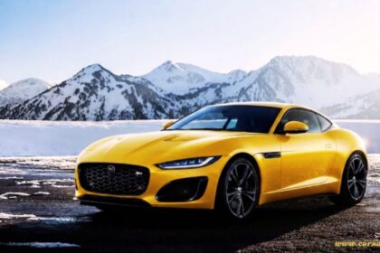 "Bright yellow Jaguar F-Type R coupe parked on a snowy road with mountains in the background."