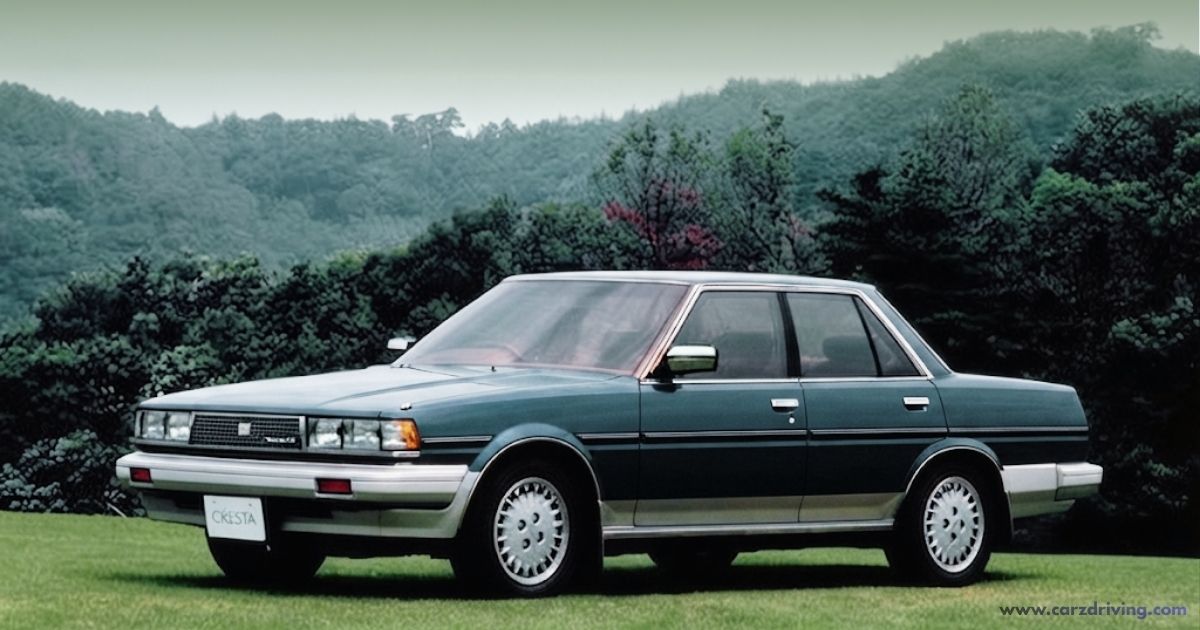 "A side-profile view of a dark teal vintage Toyota Cresta sedan parked on a grassy field with a lush, forested hill in the background."