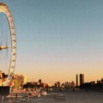 A view of the London Eye observation wheel on the banks of the River Thames at dusk, with the Houses of Parliament and Big Ben along the skyline and the text "020 Number" in the top left corner.