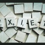Wooden letter tiles spelling out the word "anzieti" arranged across a background scattered with blank wooden tiles.