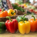 Assorted colorful bell capsicums in red, yellow, orange, green, and purple on a wooden table.