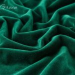 A rich emerald green velvet fabric draped in soft, deep folds with a subtle sheen, featuring the words "Emerald Green" written in elegant script in the upper-left corner.