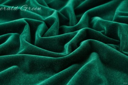 A rich emerald green velvet fabric draped in soft, deep folds with a subtle sheen, featuring the words "Emerald Green" written in elegant script in the upper-left corner.