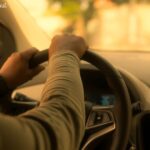 Driver holding the steering wheel of a car from a first-person perspective, illustrating a guide on how long is a driving test takes.