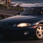 Dark blue Toyota Soarer coupe driving on a coastal road at sunset.