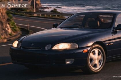 Dark blue Toyota Soarer coupe driving on a coastal road at sunset.
