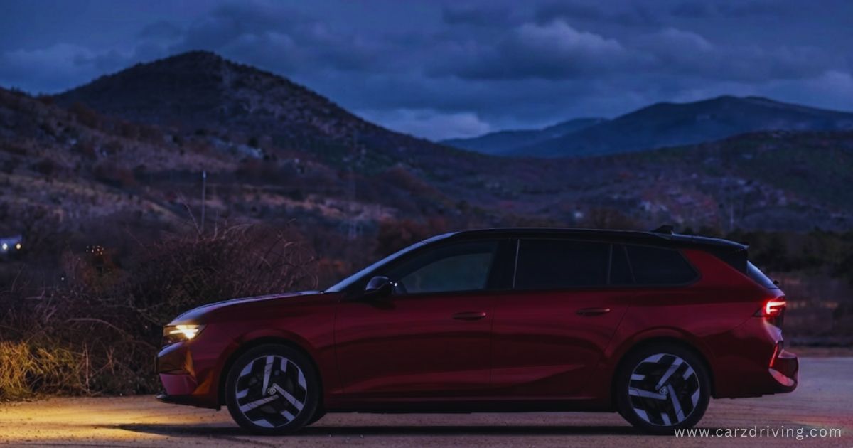 Side profile of a dark red Astra Sports Tourer parked outdoors under a dramatic night sky with mountain backdrop.
