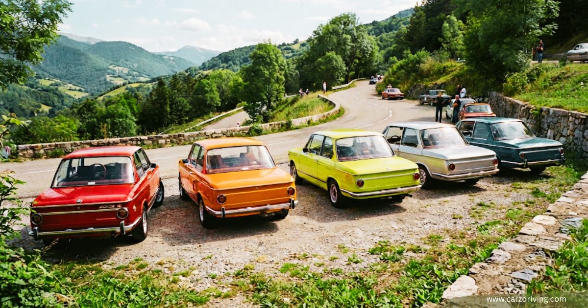 Colorful lineup of vintage BMW 2002 cars sedans parked along a scenic mountain road during a classic car rally.