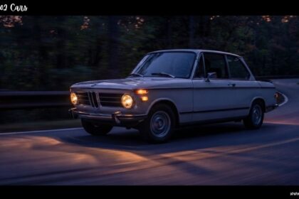 Vintage BMW 2002 cars sedan with headlights turned on driving along a quiet road at twilight.