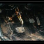Close-up view of a worn car clutch pedal mechanism inside a vehicle footwell showing potential mechanical wear causing a clutch pedal sticking