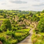 High-angle view of a quaint countryside in British with stone cottages and a church tower nestled in lush green rolling hills.