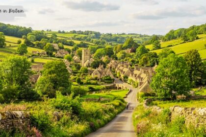 High-angle view of a quaint countryside in British with stone cottages and a church tower nestled in lush green rolling hills.