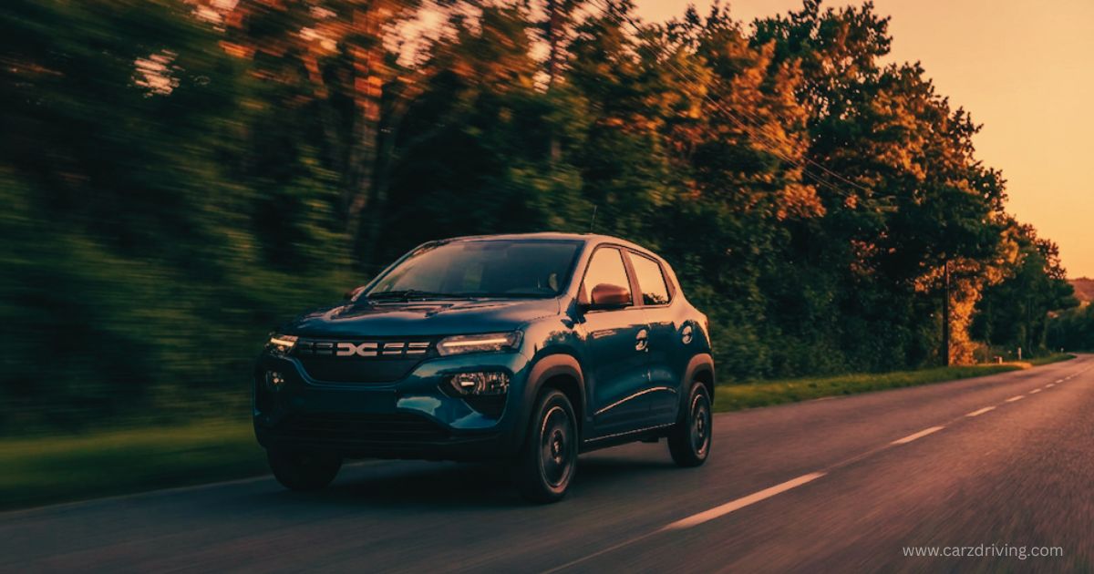 Blue Dacia Spring electric car driving along a scenic country road at sunset.