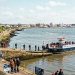 The Knott End–Fleetwood Ferry, filled with passengers, docked at a stone slipway along a coastal promenade.