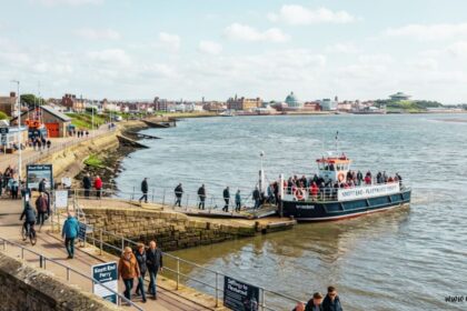 The Knott End–Fleetwood Ferry, filled with passengers, docked at a stone slipway along a coastal promenade.