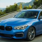 Blue BMW M140i performance hatchback driving along a scenic mountain road