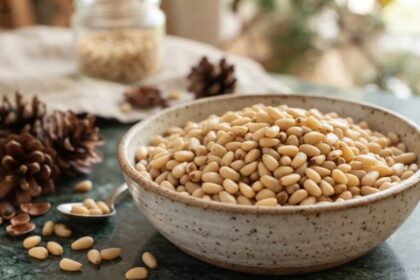 A ceramic bowl filled with raw pine nut nuts on a table next to pinecones.