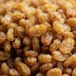 Close-up of a pile of golden-brown sultanas raisins on a wooden surface.