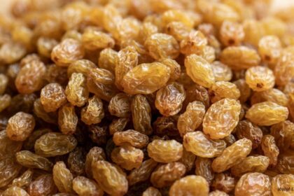 Close-up of a pile of golden-brown sultanas raisins on a wooden surface.