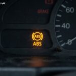 Illuminated yellow anti lock brake system warning light on a car dashboard cluster.